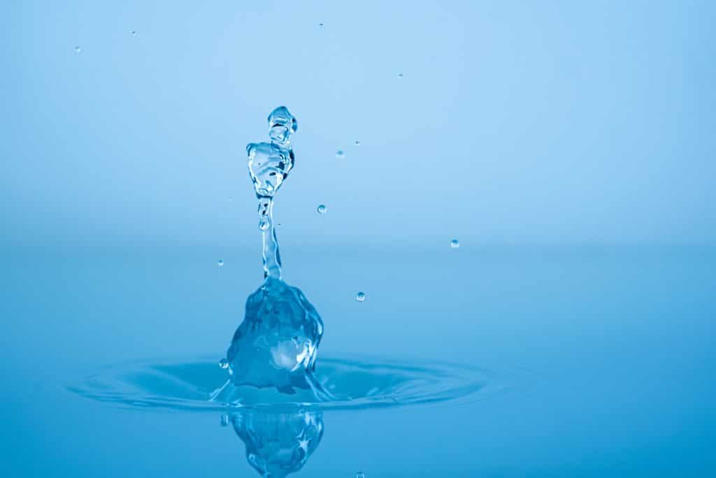 Water drop splashing into blue water surface